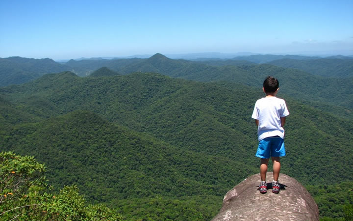 Criança na ponta de uma pedra grande, olhando para o Morro do Spiytkopf em Blumenau Criança na ponta de uma pedra grande, olhando para o Morro do Spiytkopf em Blumenau