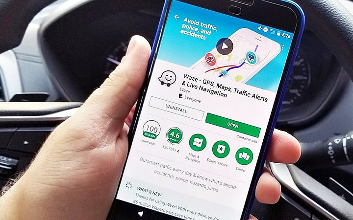 Pessoa em carro segurando smartphone na tela de instalação do aplicativo waze Pessoa em carro segurando smartphone na tela de instalação do aplicativo waze