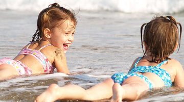 Duas crianças deitada na areia da praia