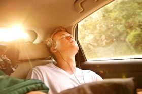 Rapaz dormindo no carro e ouvindo música durante a viagem longa