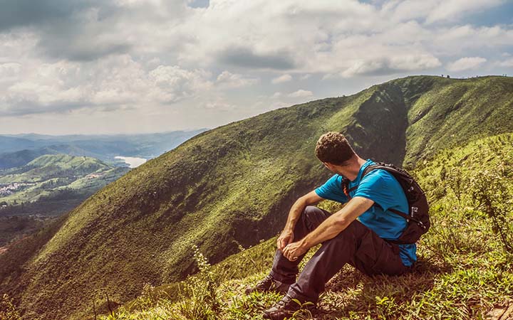 Homem sentado no alto da montanha - Viajar Sozinho